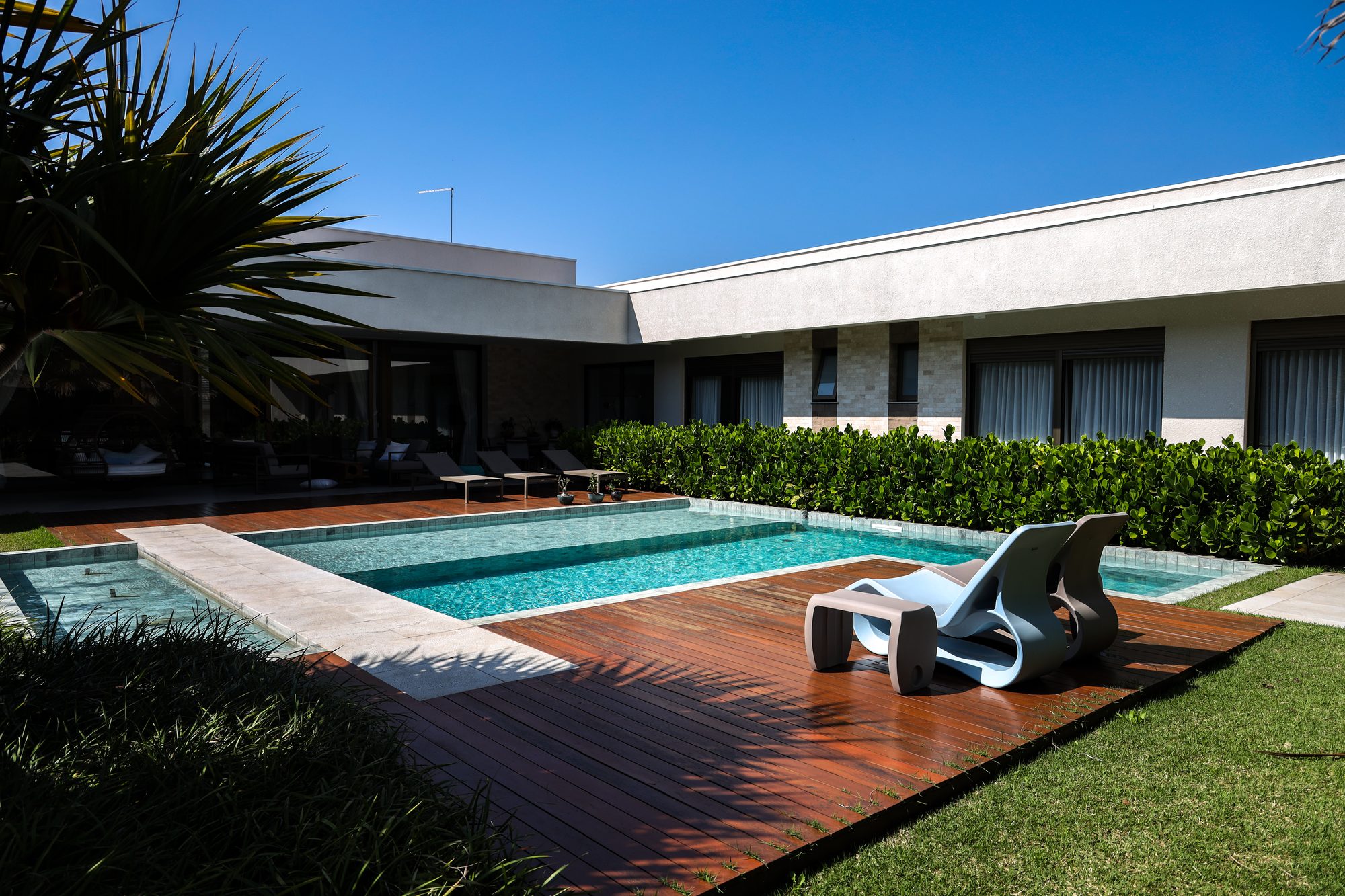 Piscina em formato recortado com prainha e diferentes profundidades, cercada por deck de madeira