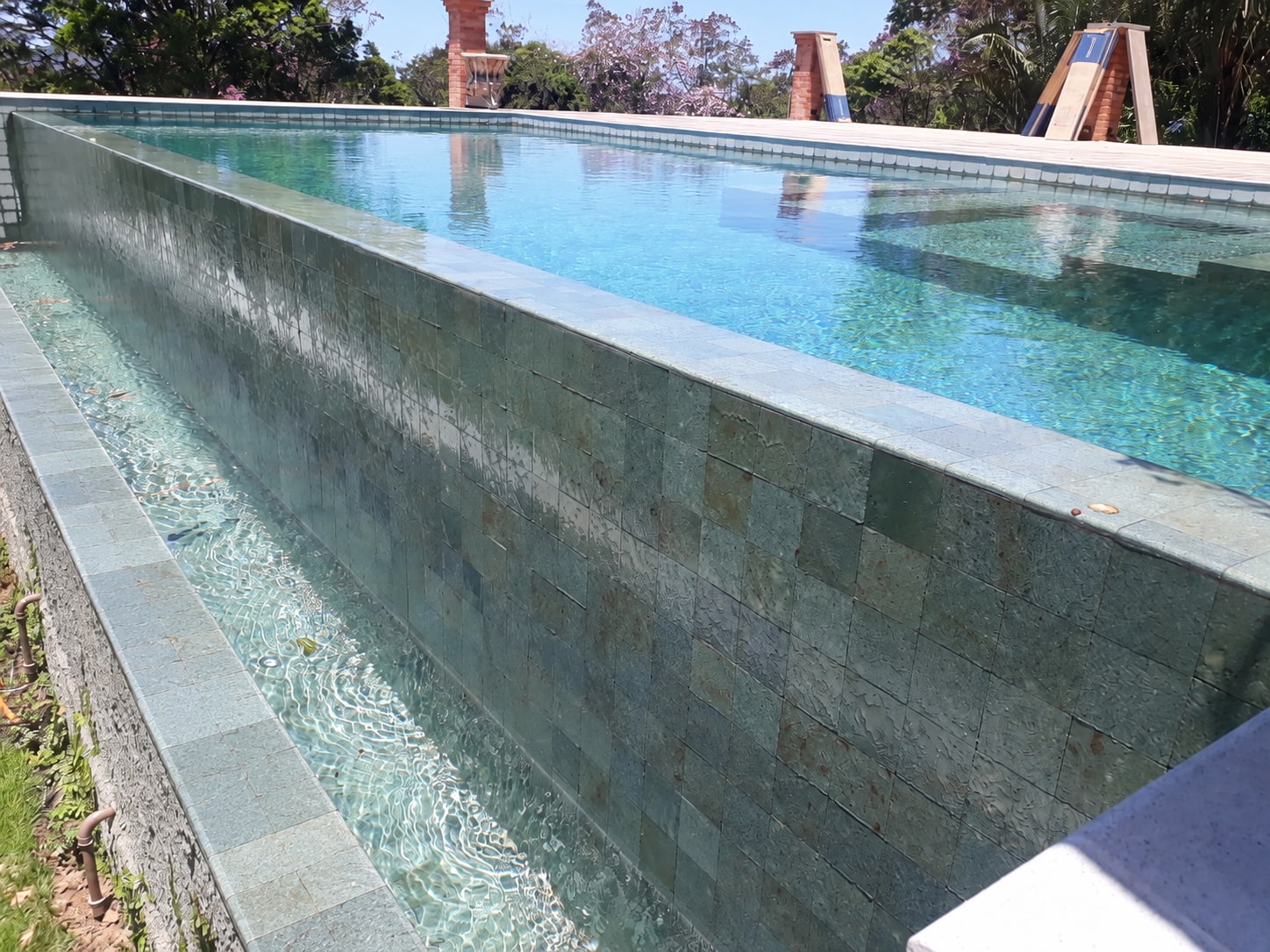 Piscina com borda infinita, parede e acabamento da calha em pedra natural
